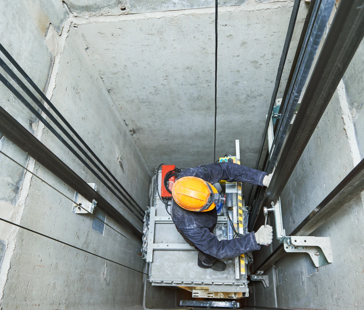 Certified elevator mechanic working on guide rails inside an elevator shaft